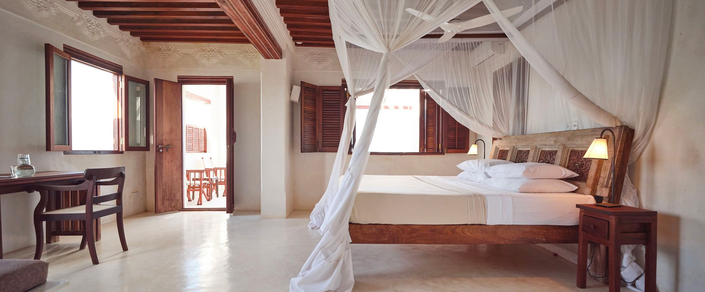 chambre de la villa à Shella Beach sur l’île de Lamu au Kenya avec lit à baldaquin et tête de lit sculptée